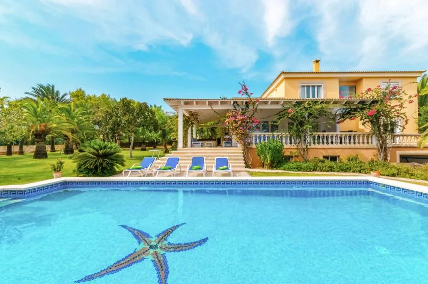 A swimming pool with a star-shaped tile design sits in front of a house and garden.