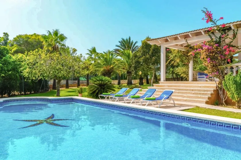 Una piscina junto a un patio con asientos y enredaderas con flores.