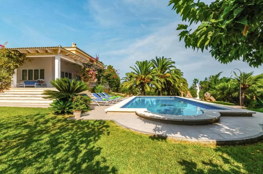 An outdoor swimming pool sits beside a garden and a house.