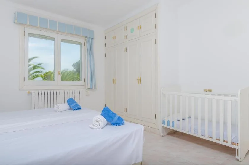 A bright bedroom with a bed, a window, and a white crib.