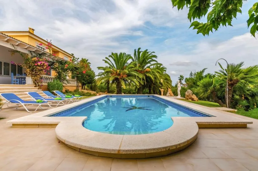 An outdoor swimming pool sits beside a landscaped garden and sun loungers.