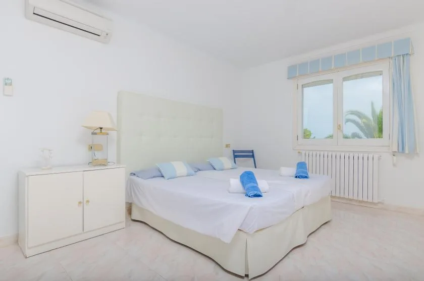 A bright bedroom with a bed, bedside cabinet, and a window.