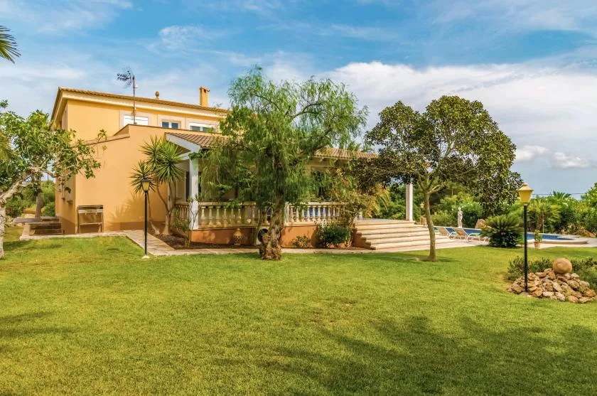 A landscaped garden with a broad lawn, trees, and a swimming pool beside a house.