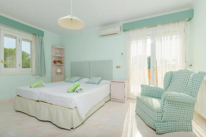 A bright bedroom with a double bed and a plaid armchair beside the window.