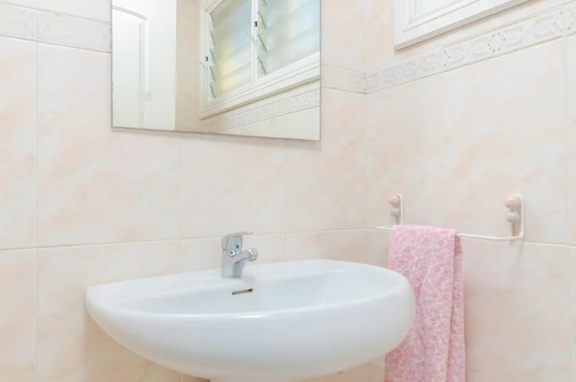 A bathroom sink sits below a mirror, with a pink towel hanging nearby.