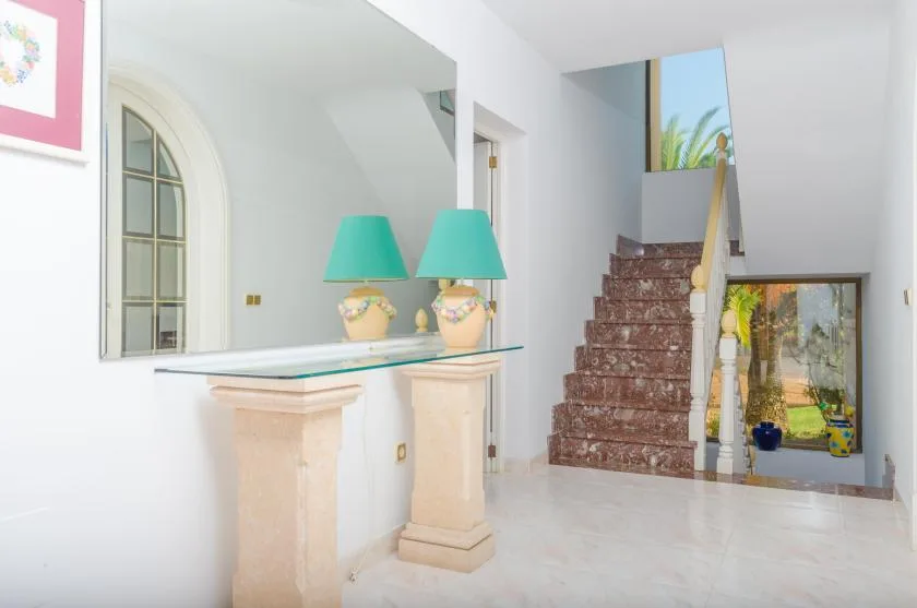 A bright interior shows a staircase beside a glass-topped console table.