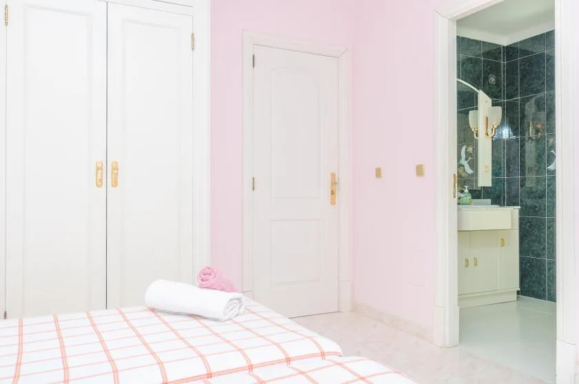 A bedroom with a neatly made bed beside an open bathroom doorway.