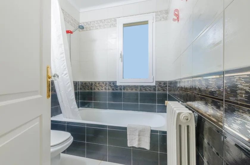 A tiled bathroom with a bathtub, shower curtain, and window.