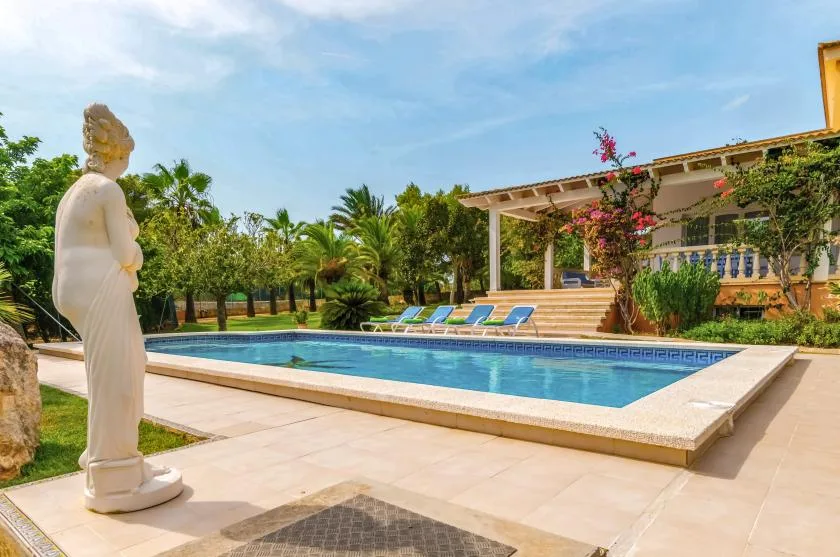 An outdoor swimming pool beside a covered patio and landscaped garden.