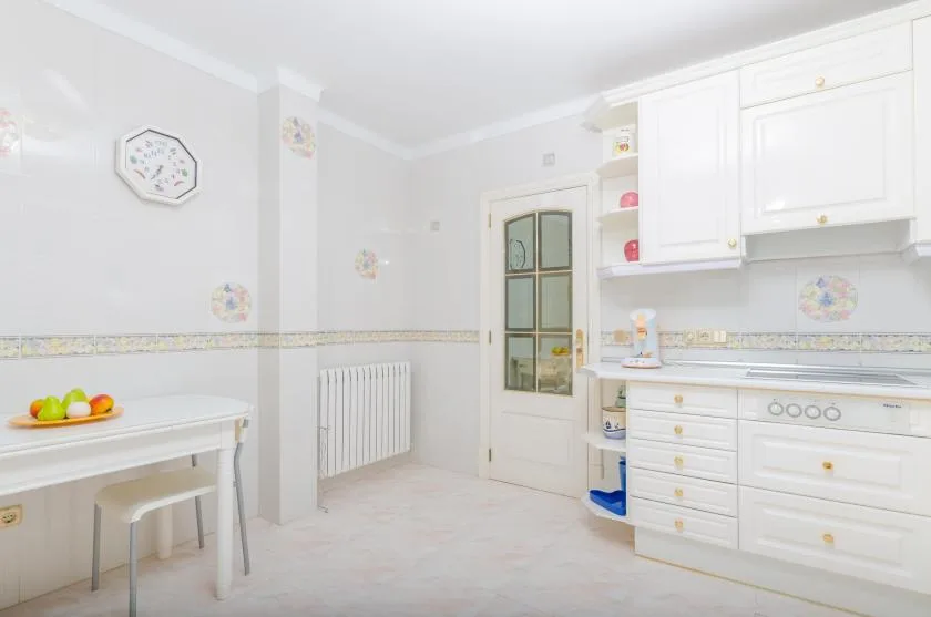 A bright kitchen with white cabinets, a stove, and a small table.