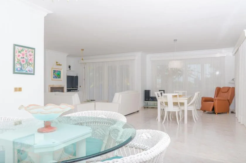 A bright living and dining room with white seating and a glass table.