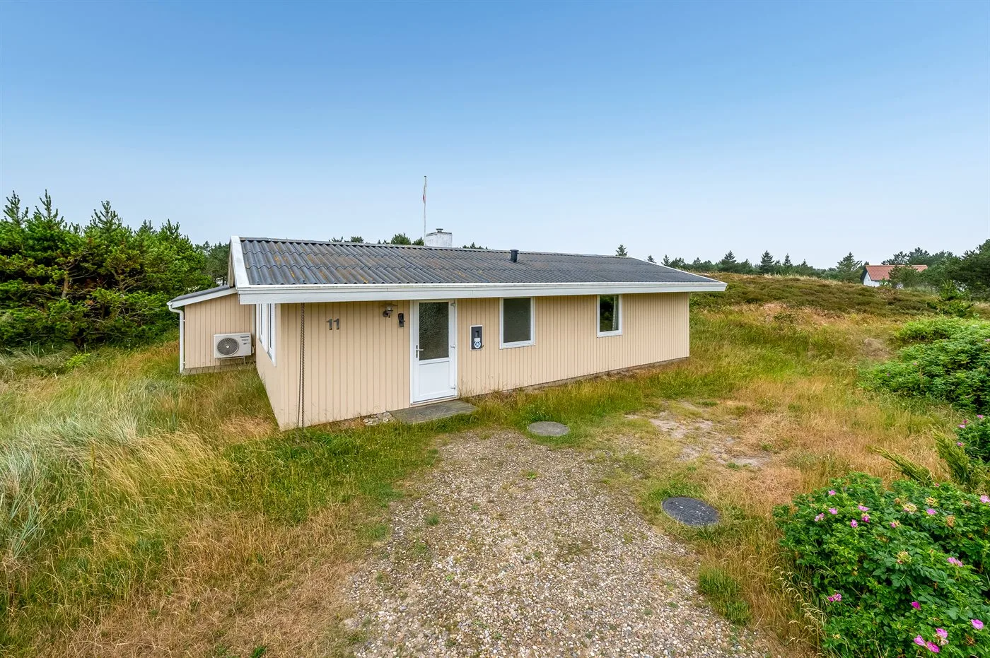 A single-story house stands beside a gravel path in open grassy surroundings.