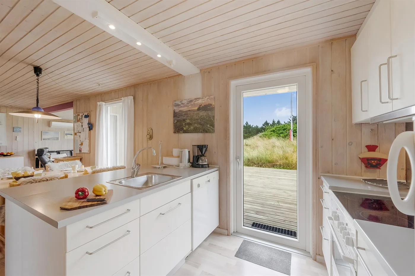 Una cocina luminosa con gabinetes blancos y una puerta de vidrio que da a una terraza.
