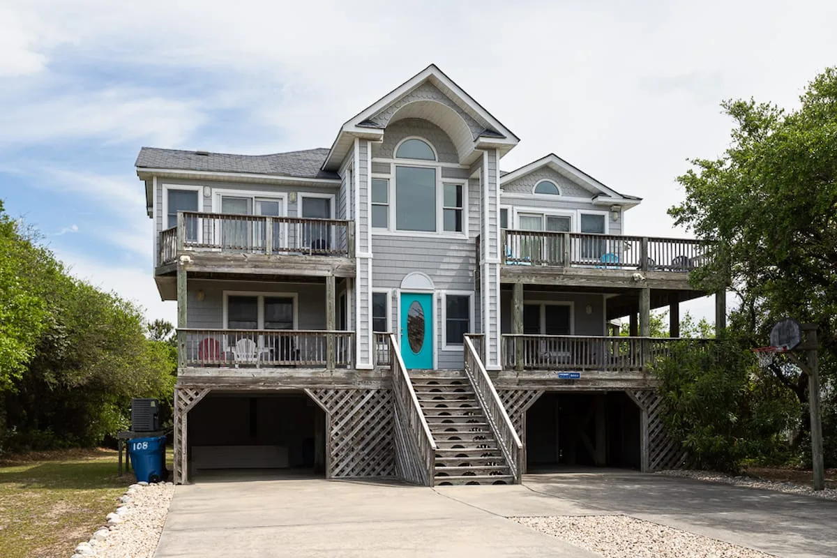 A raised coastal-style house with balconies and a central exterior staircase.