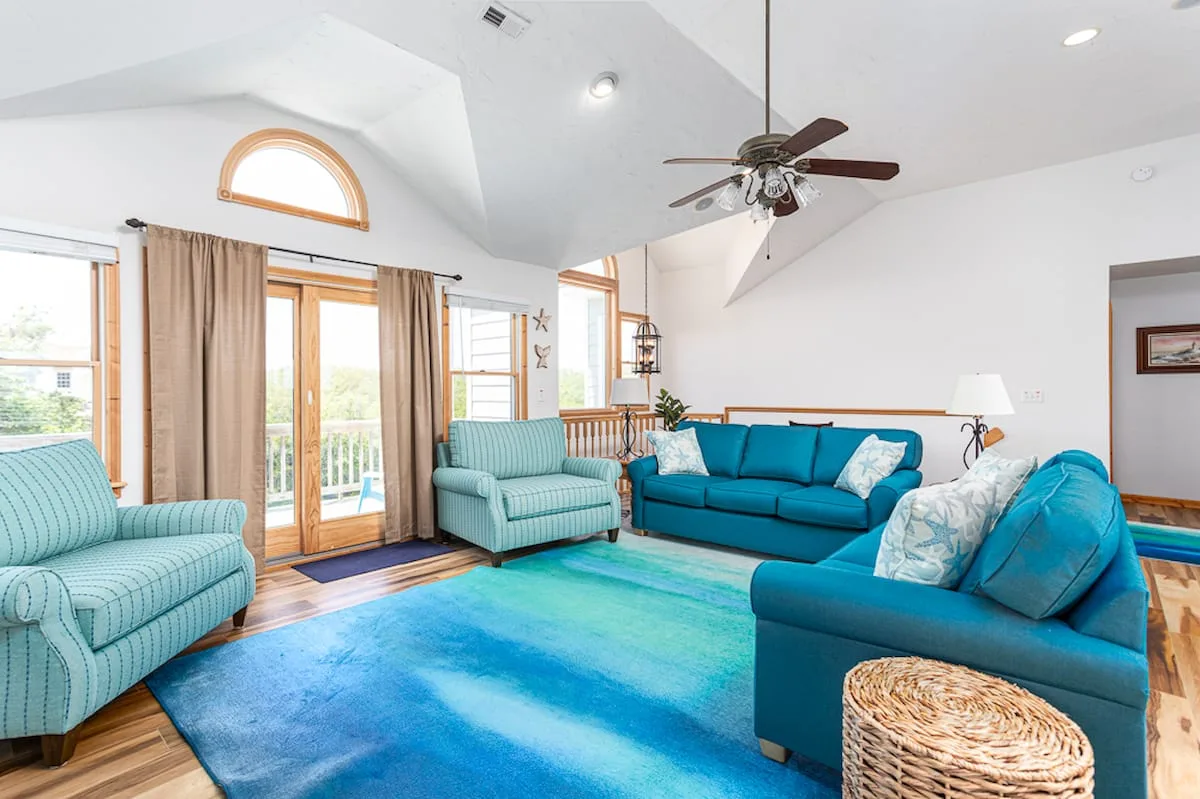A bright living room with teal seating and a large blue rug.