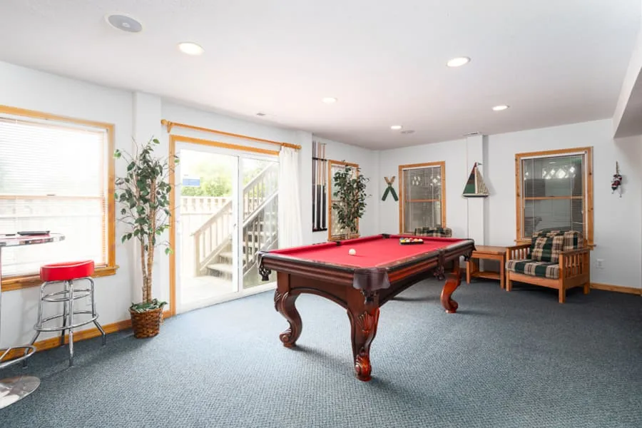 A recreation room features a pool table, a small seating area, and windows.