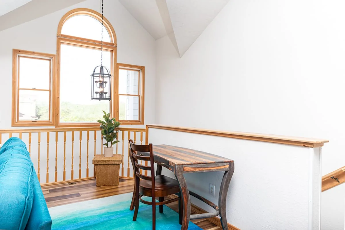 A dining area with a wooden table beside tall windows and a railing.