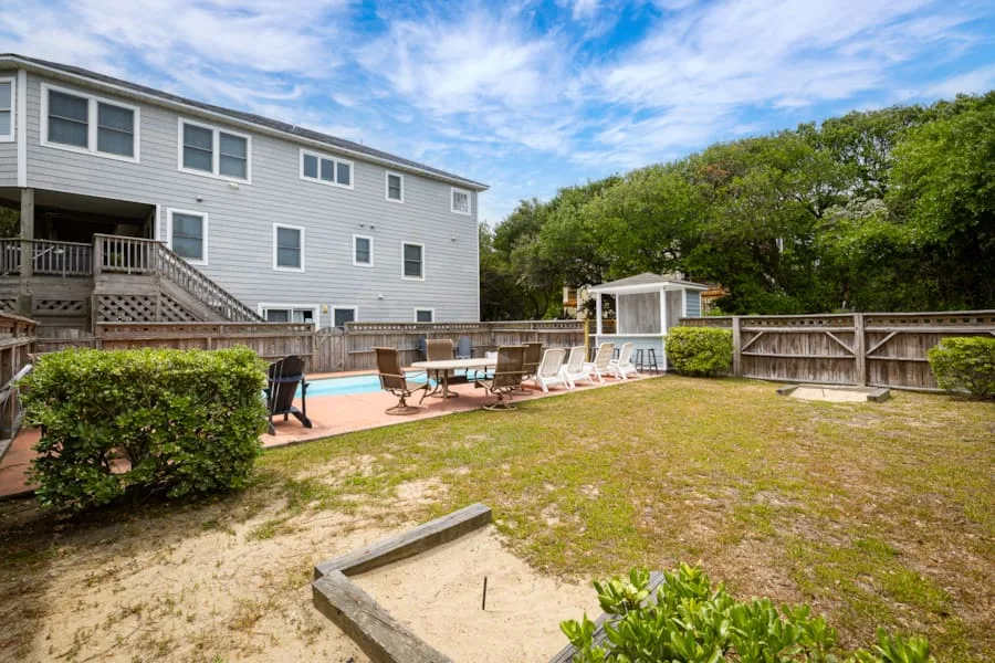 A fenced backyard patio with outdoor seating beside a large house.