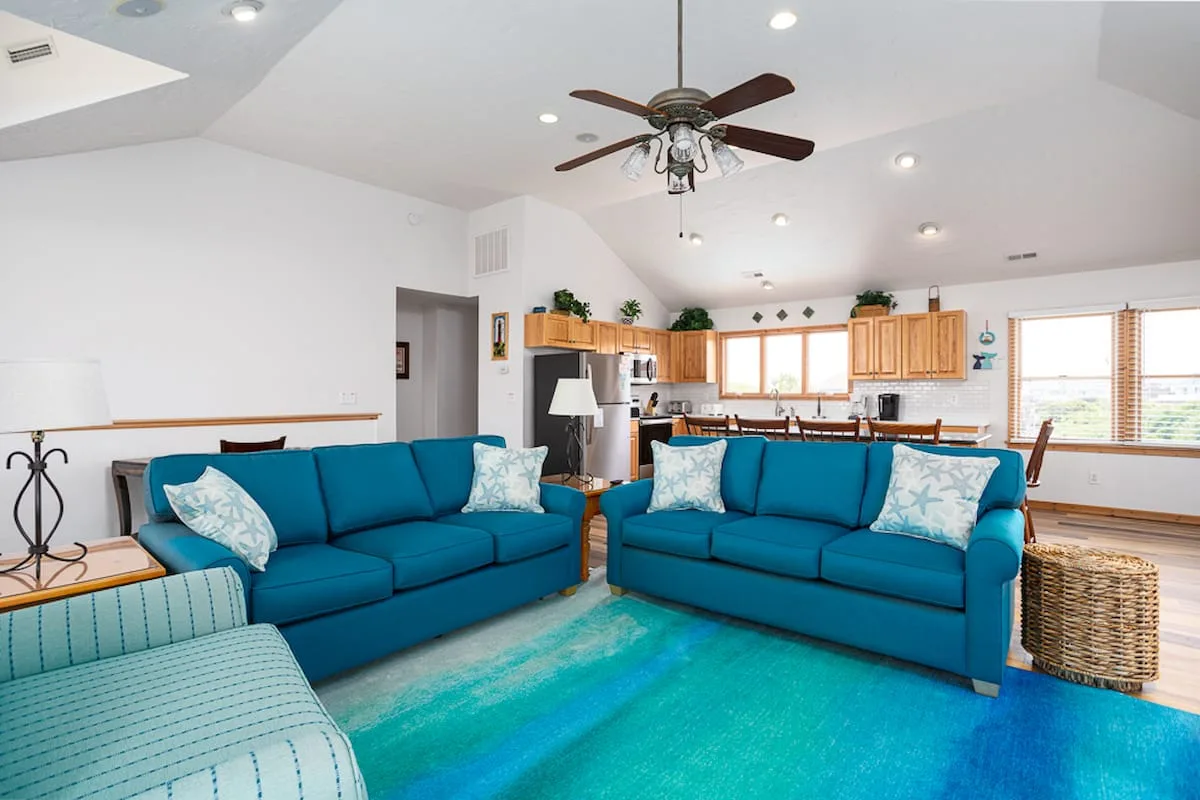 A bright living room with blue seating and an open kitchen in the background.