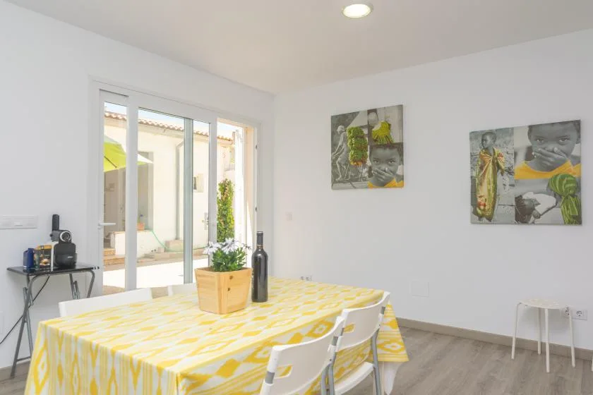 Un comedor luminoso con un mantel estampado amarillo junto a grandes ventanas.