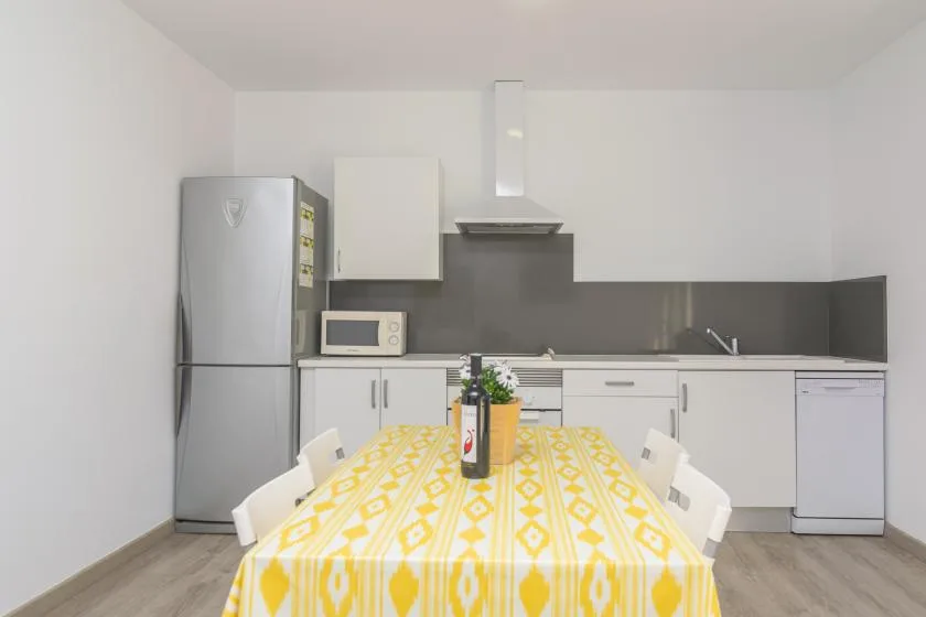 Una cocina luminosa con armarios blancos y una mesa de comedor estampada en amarillo.
