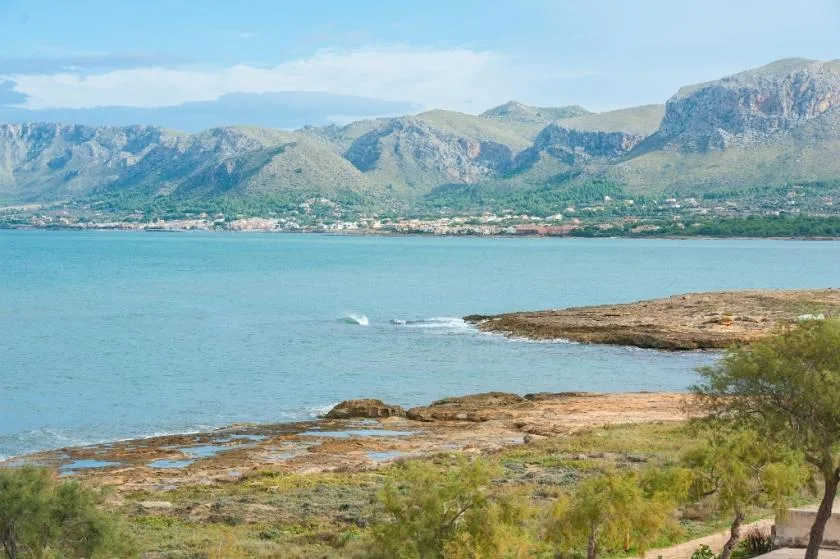 A coastal bay with low rocky shoreline and mountains across the water.