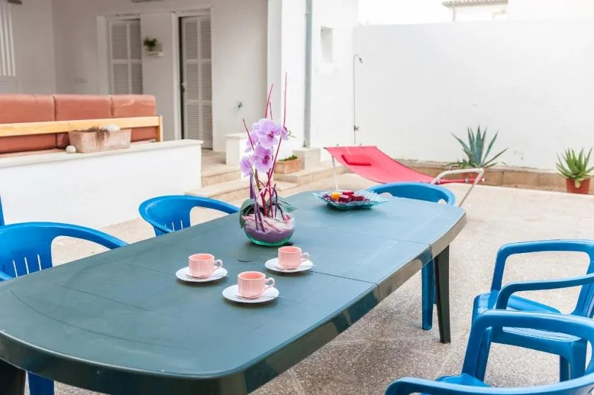 An outdoor patio table is set with cups beside blue seating and a small pool.