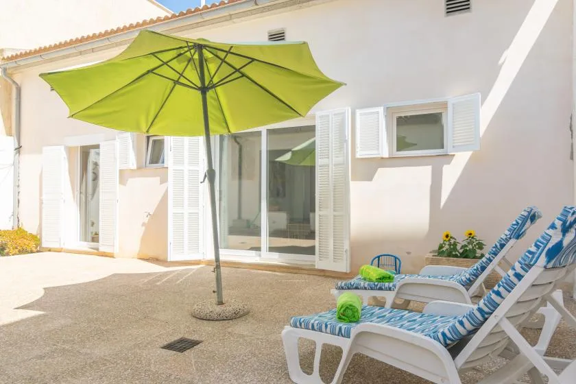 A sunny patio with a green umbrella, lounge seating, and doors opening onto the house.