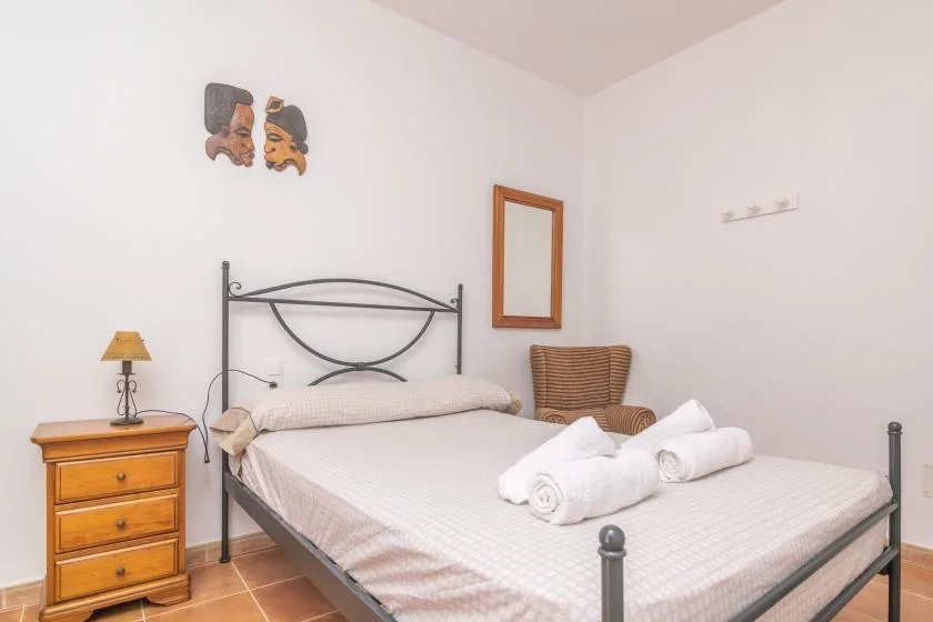 A bedroom with a metal bed, folded towels, and a wooden bedside table.