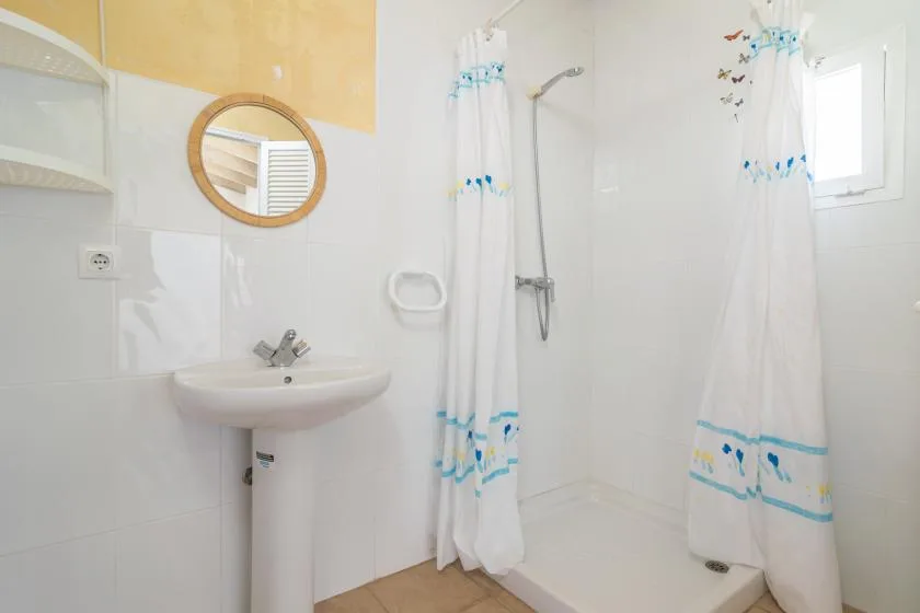 A bright bathroom with a pedestal sink, shower, and patterned curtains.