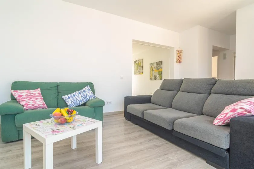 Una sala de estar con asientos grises y verdes alrededor de una mesa de centro blanca.