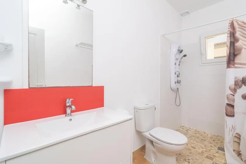 A bright bathroom with a long sink, toilet, and shower.