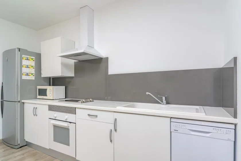 A bright kitchen with white cabinets, a refrigerator, and a long countertop.