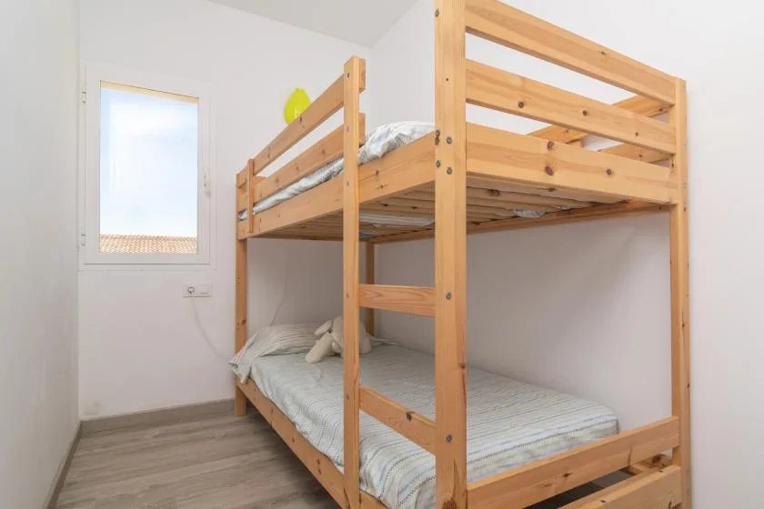 A wooden bunk bed with striped bedding sits beside a window in a bedroom.