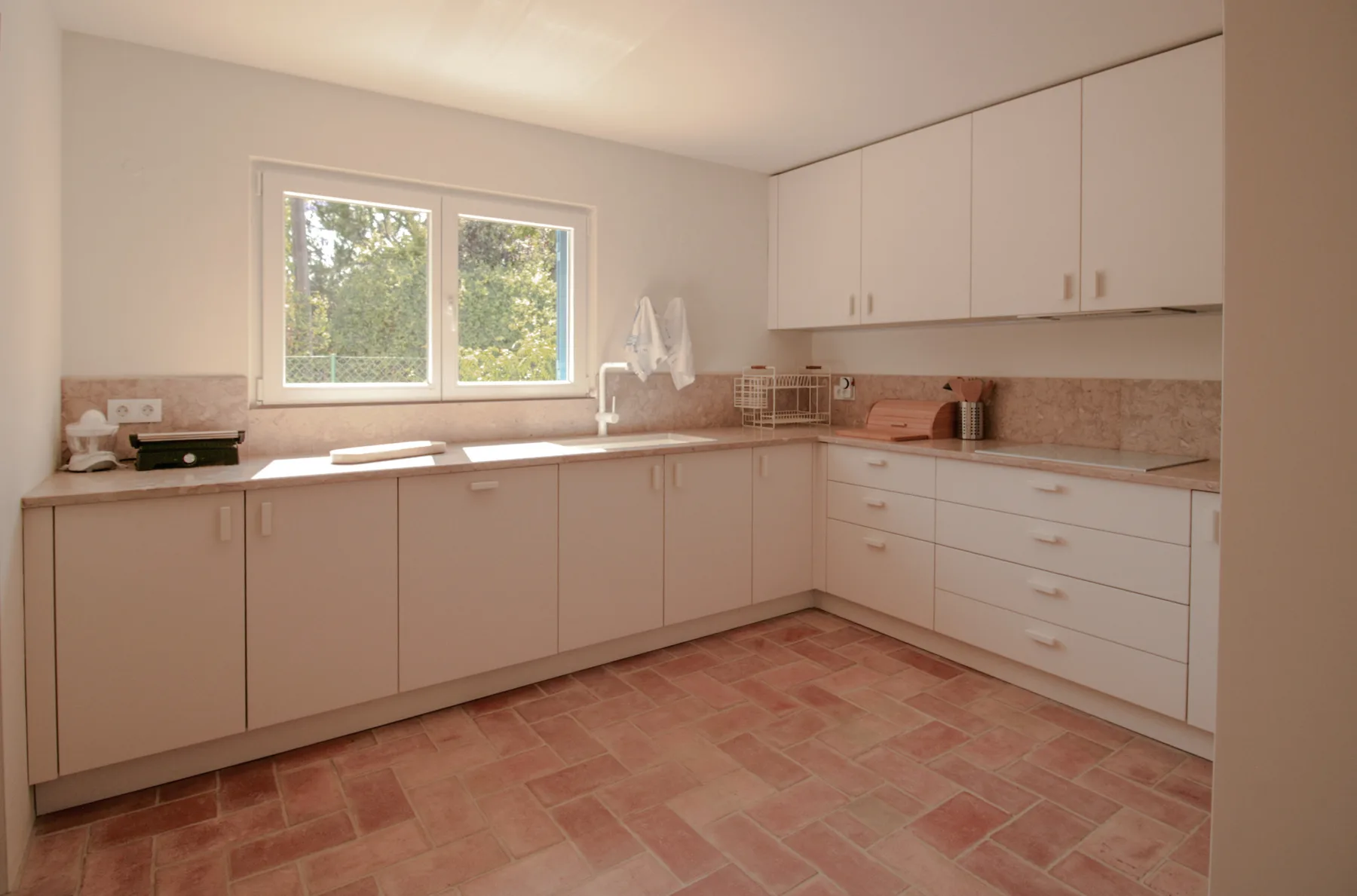 Una cocina luminosa con armarios claros, encimeras de azulejos y una ventana.