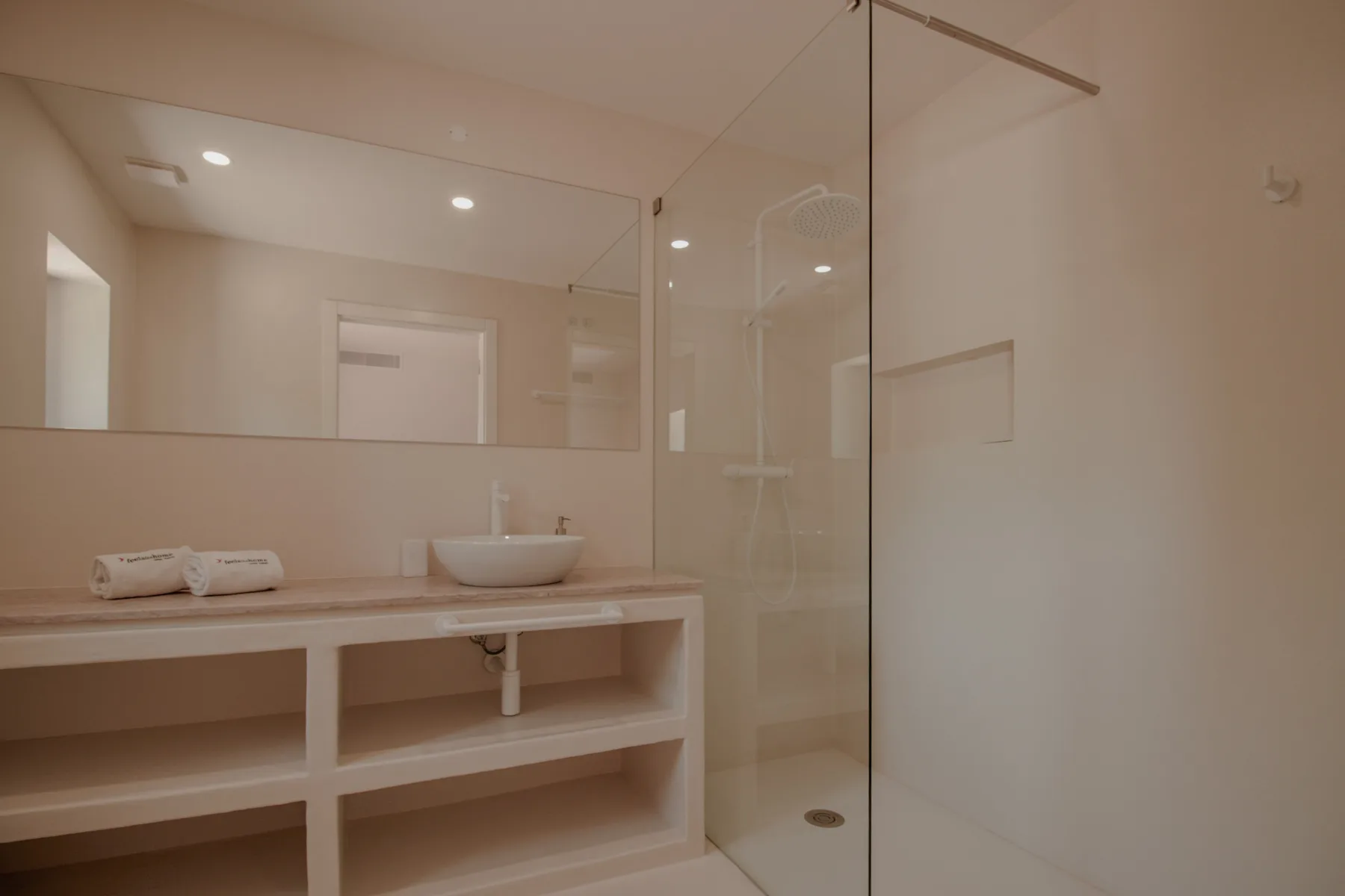 Un baño luminoso con un tocador largo, lavabo sobre encimera y ducha de cristal.