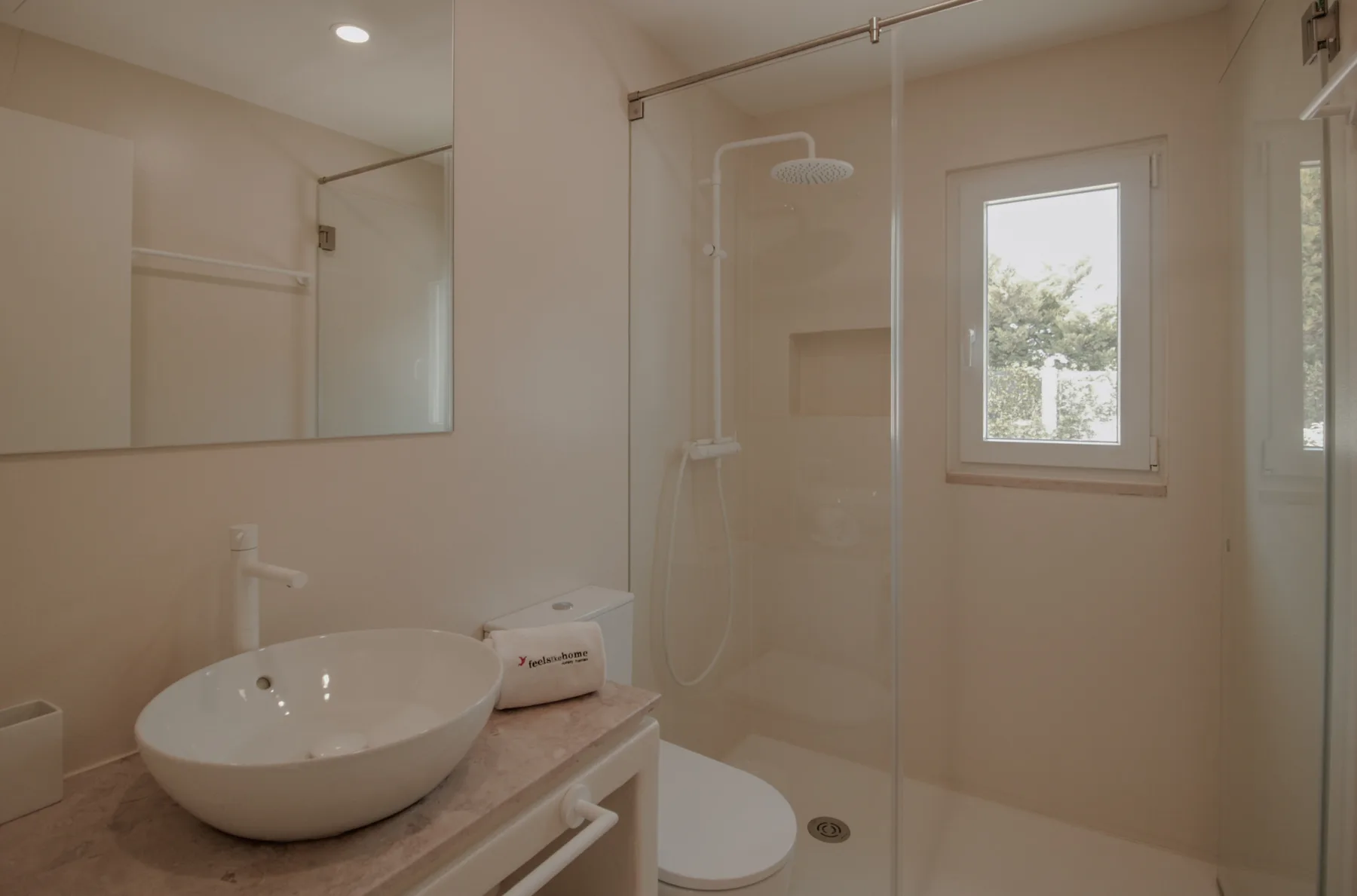 Un baño luminoso con lavabo sobre encimera, espejo grande y ducha de vidrio.