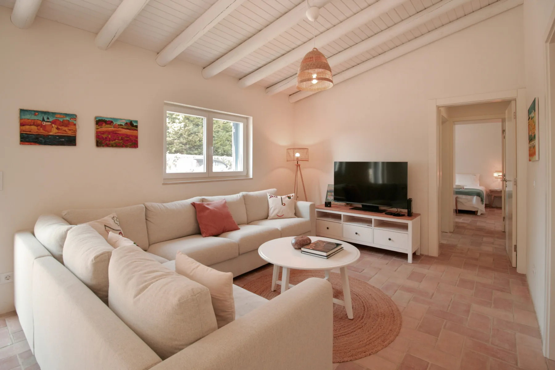 Sala de estar con asientos claros, televisor y mesa de centro redonda.