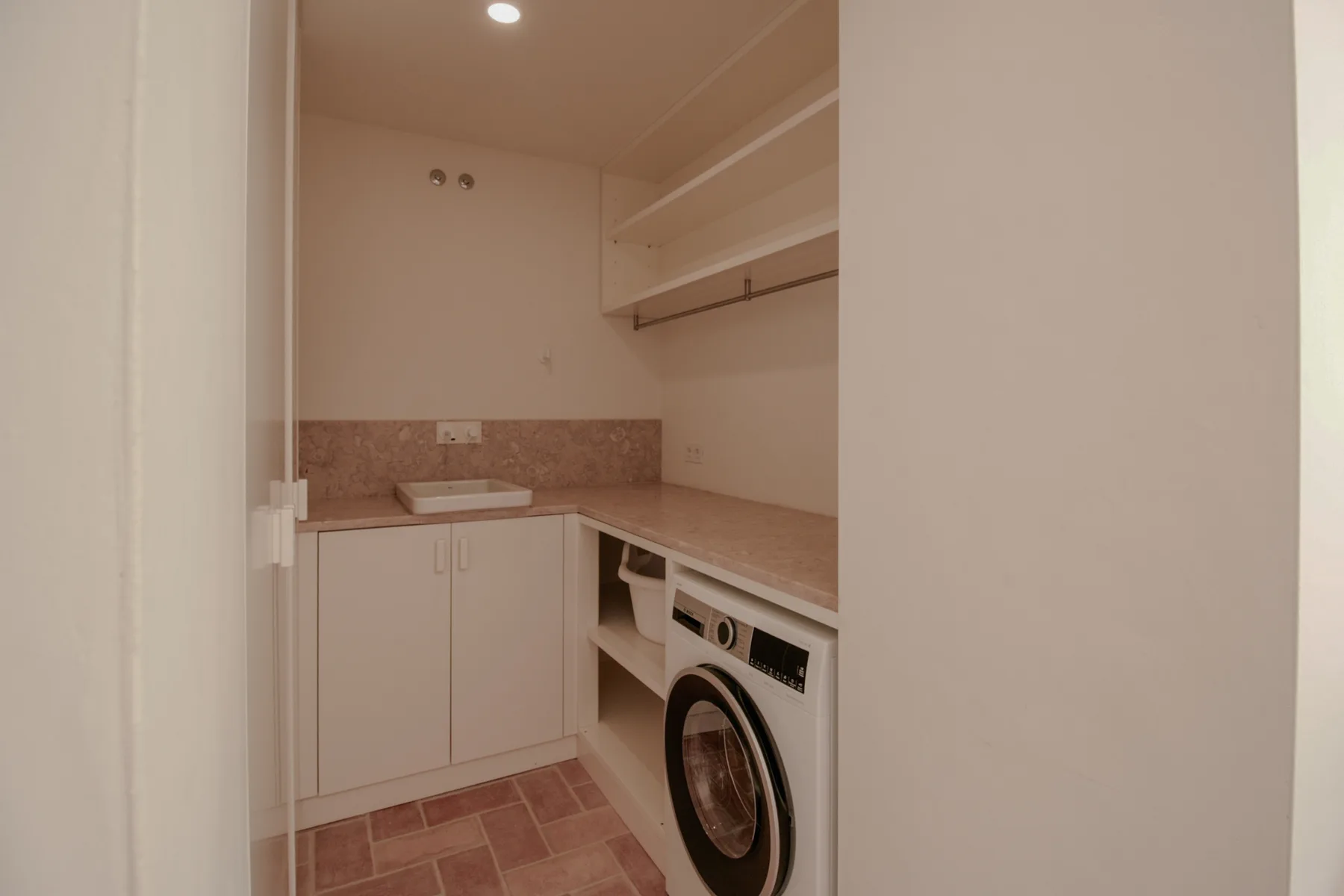 Un cuarto de lavandería con una lavadora bajo la encimera.