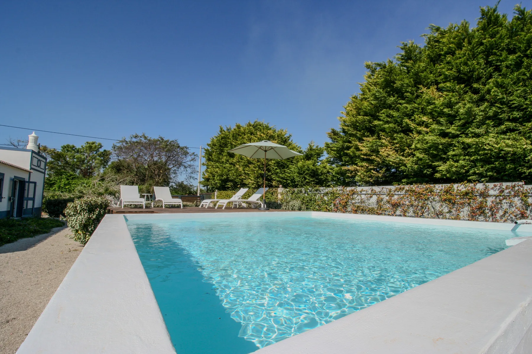 Una piscina al aire libre con asientos, una sombrilla y árboles.