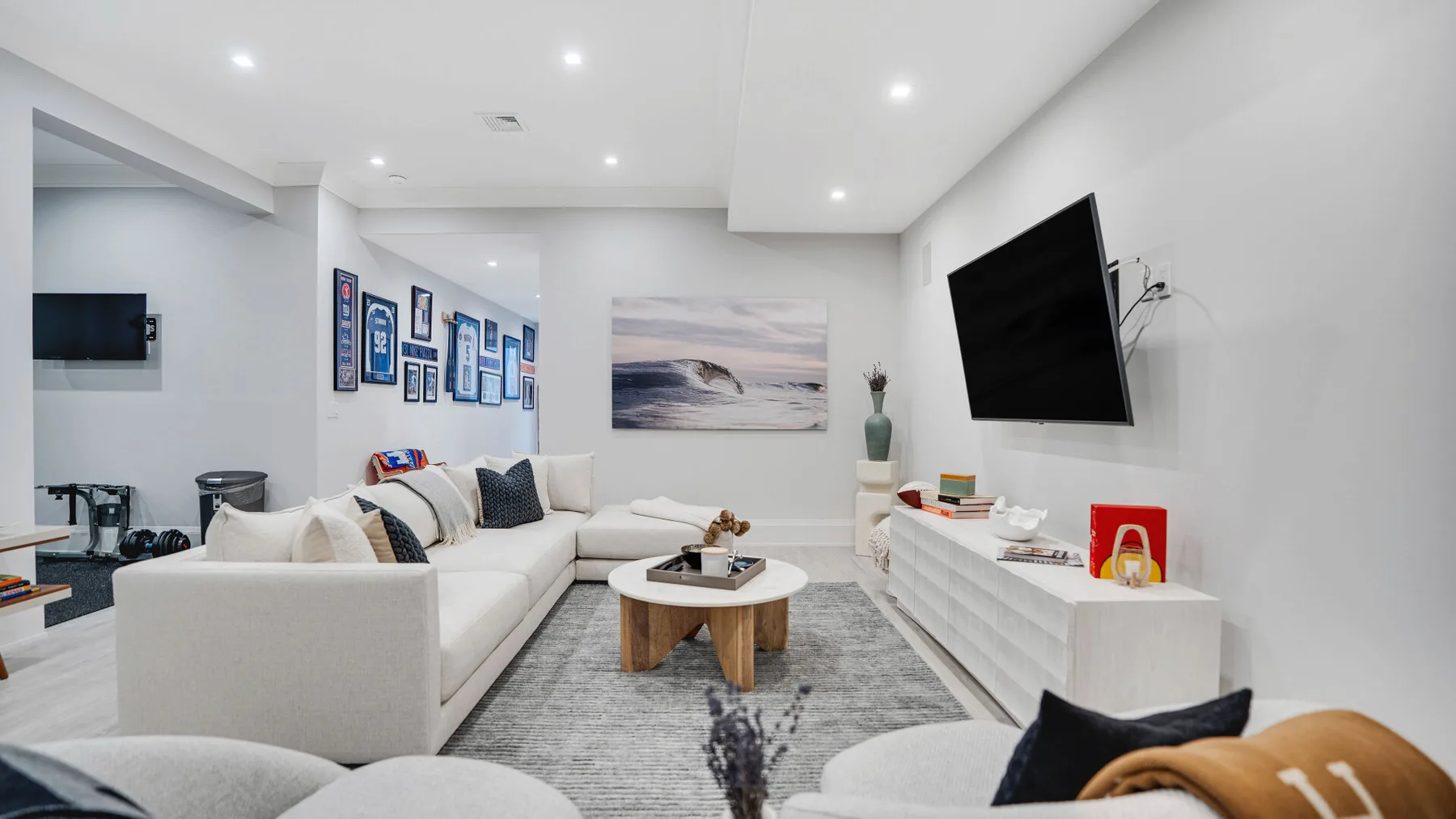 Una sala luminosa con asientos blancos, una mesa de centro y un televisor en la pared.