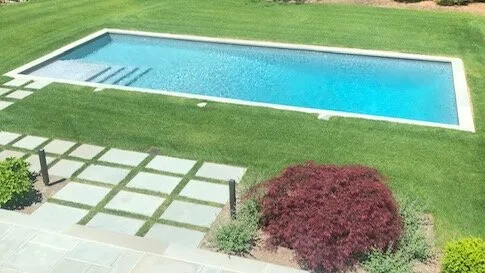 Una piscina está en un césped verde junto a un sendero pavimentado.