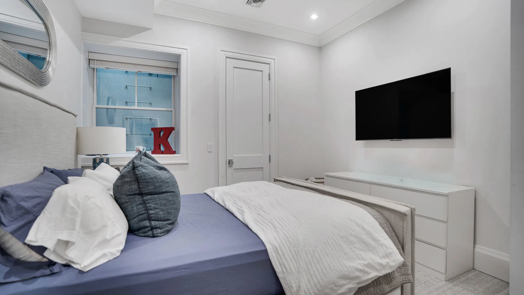 Un dormitorio con una cama, un televisor montado en la pared y una ventana.