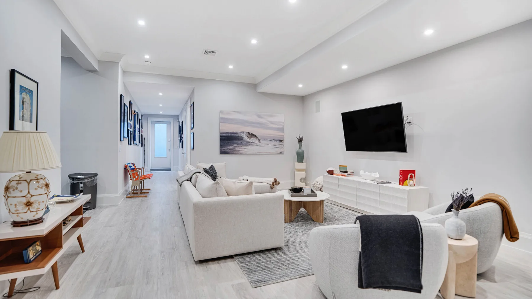Una sala luminosa con asientos claros, un televisor en la pared y cuadros.