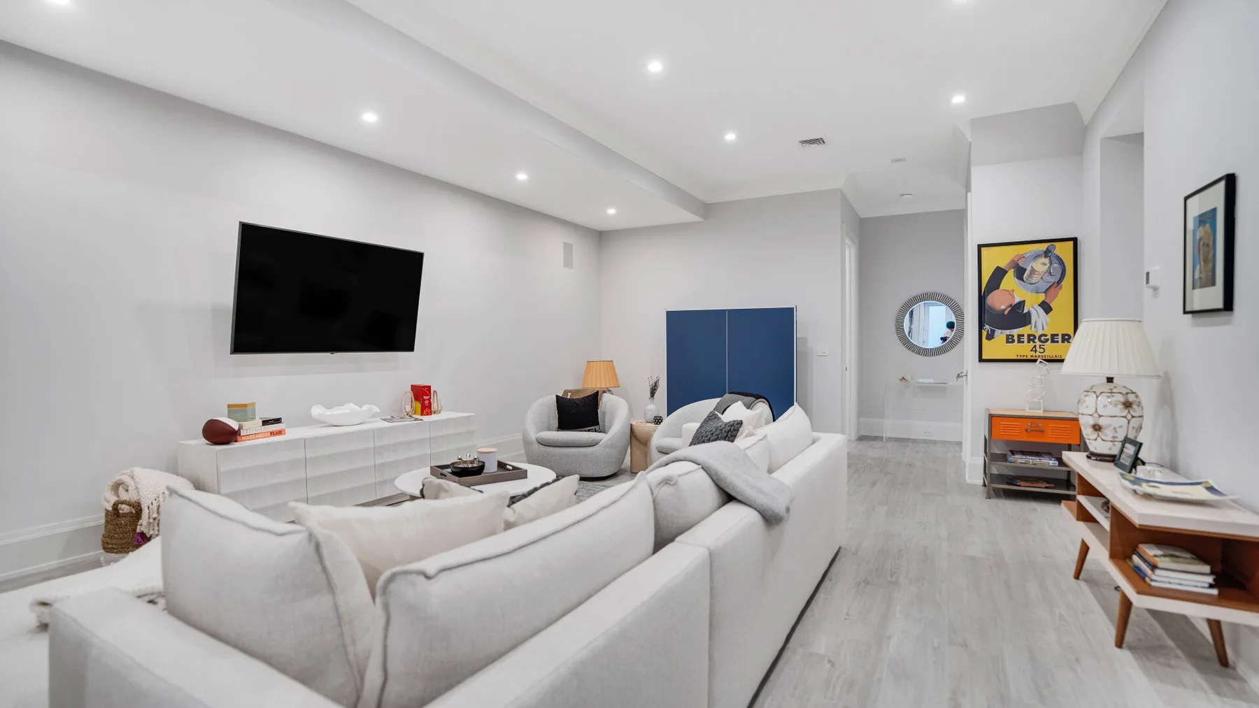 Una sala luminosa con asientos claros, un televisor en la pared y arte colorido.