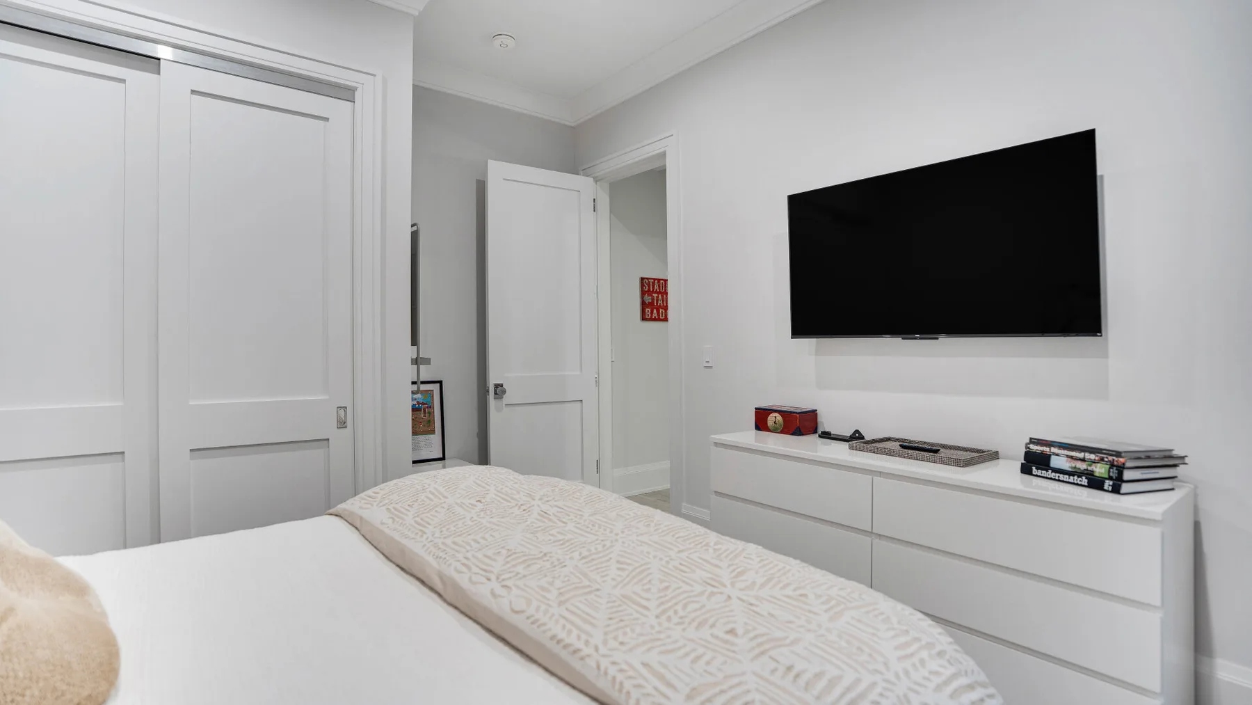 Un dormitorio con una cama, un televisor en la pared y una cómoda.