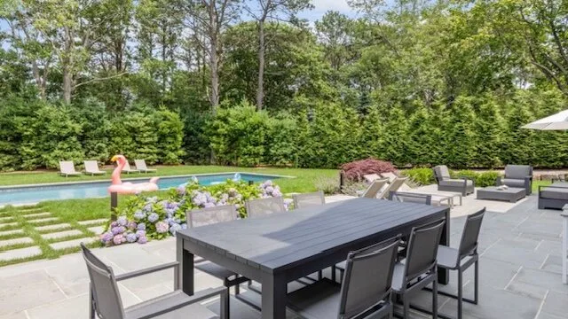 Una zona de comedor al aire libre con una mesa oscura y asientos junto a una piscina.