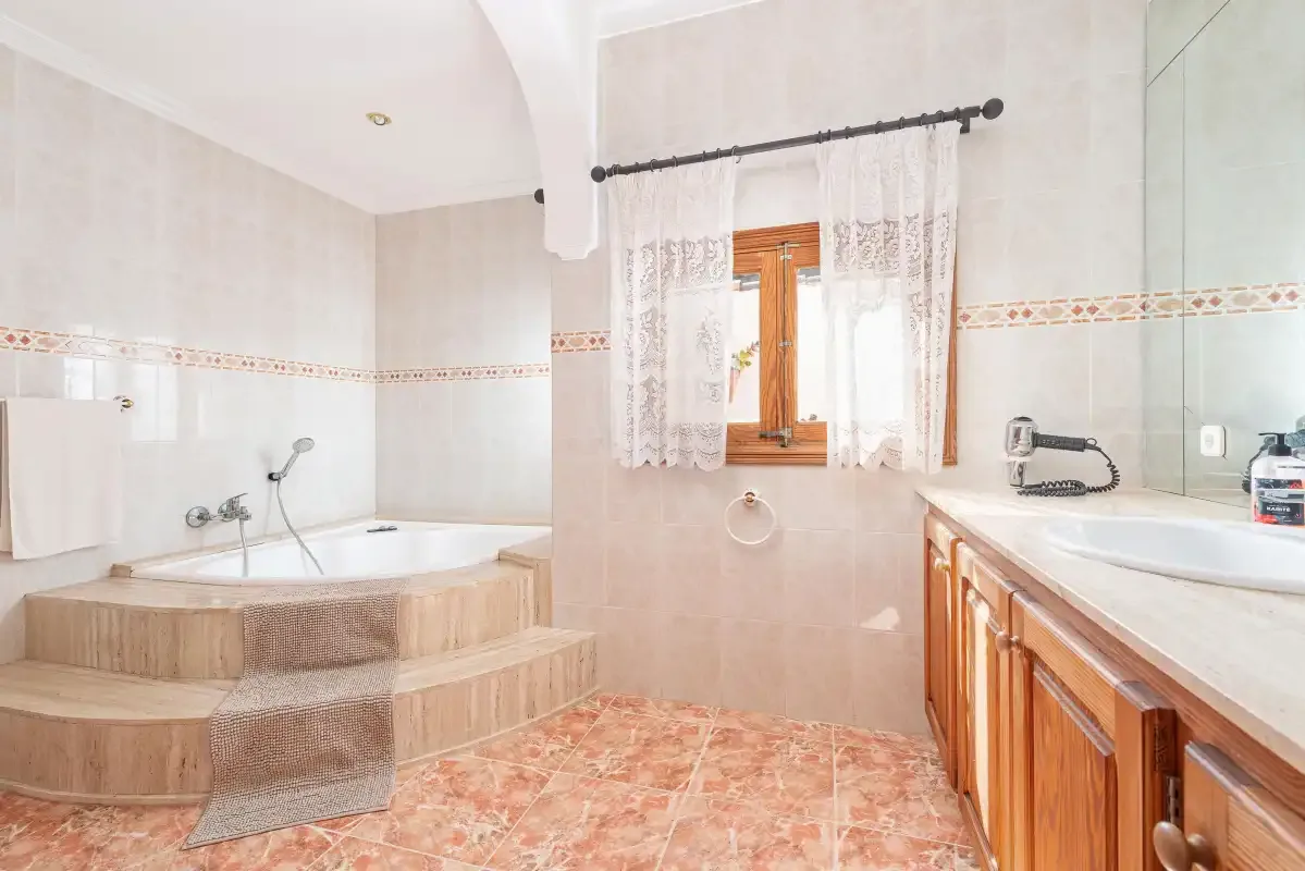 A bathroom with a raised corner bathtub, window, and wooden vanity.