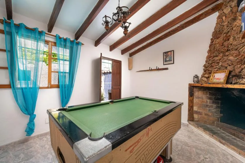 A game room features a green pool table beneath exposed wooden ceiling beams.