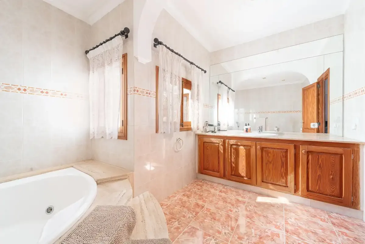 A tiled bathroom with a bathtub and a long wooden vanity beneath a mirror.
